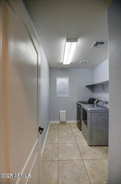 clothes washing area featuring washer and clothes dryer, light tile patterned floors, and a textured ceiling