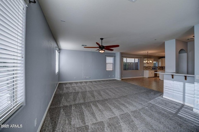 unfurnished living room with ceiling fan with notable chandelier and dark carpet