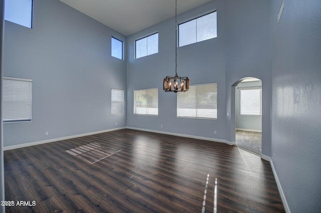 empty room featuring dark wood-type flooring, a chandelier, and a high ceiling