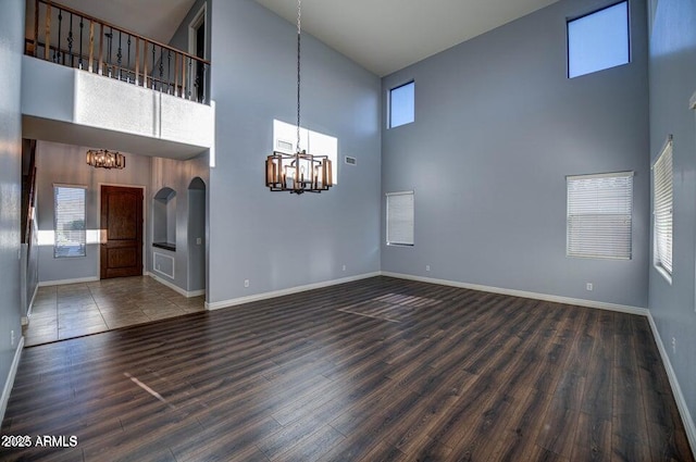 unfurnished living room featuring a notable chandelier, dark hardwood / wood-style flooring, and a towering ceiling