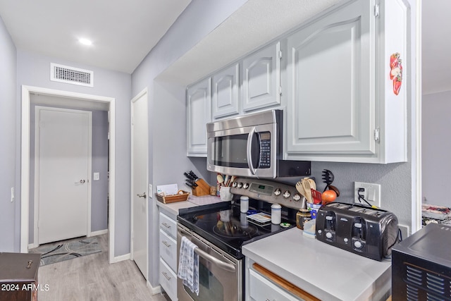 kitchen with appliances with stainless steel finishes, light hardwood / wood-style floors, and white cabinetry