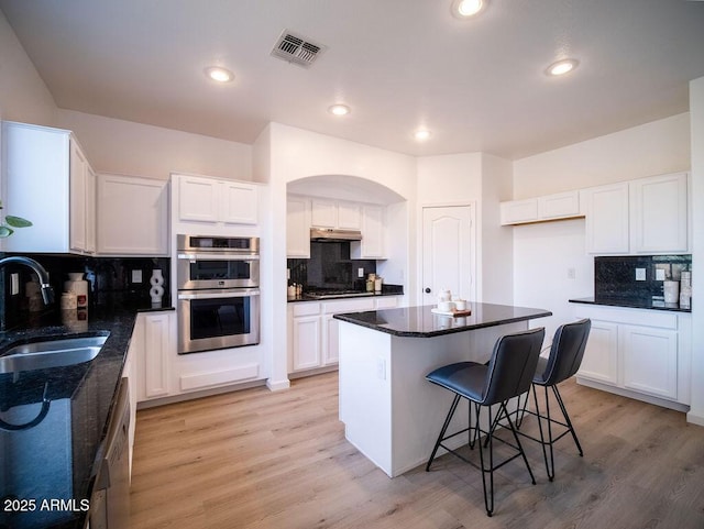 kitchen with appliances with stainless steel finishes, a kitchen island, sink, light hardwood / wood-style floors, and white cabinetry