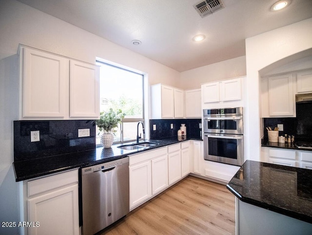 kitchen with sink, stainless steel appliances, backsplash, dark stone counters, and white cabinets