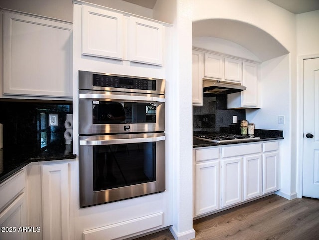 kitchen with white cabinets, backsplash, stainless steel appliances, and dark stone countertops