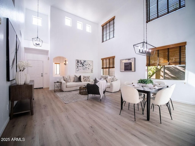 dining room with a chandelier, a towering ceiling, light hardwood / wood-style flooring, and a healthy amount of sunlight