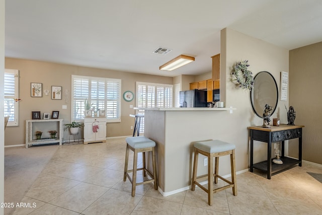 kitchen featuring a kitchen breakfast bar, light tile patterned floors, plenty of natural light, and black appliances