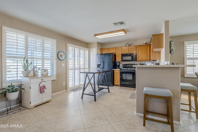 kitchen with a kitchen bar, light tile patterned floors, a healthy amount of sunlight, and black appliances