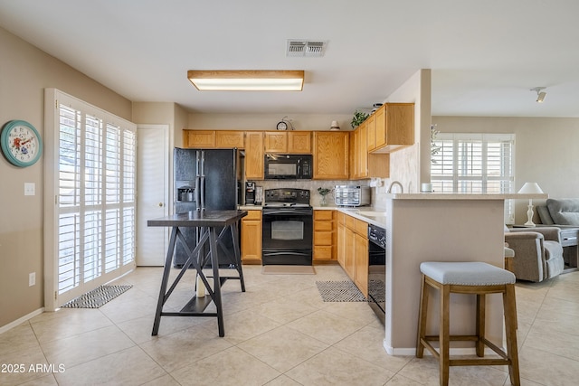 kitchen featuring backsplash, black appliances, sink, light tile patterned floors, and a kitchen bar