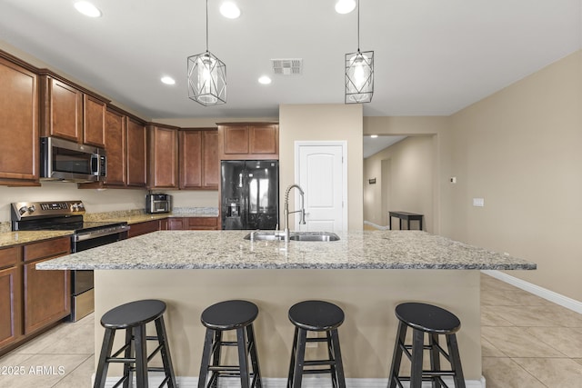 25969 W Tina Ln, Buckeye, AZ 85396 - kitchen with stainless steel appliances, light tile patterned flooring, a kitchen bar, an island with sink, and decorative light fixtures