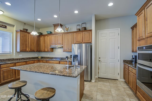 kitchen featuring brown cabinetry, an island with sink, appliances with stainless steel finishes, under cabinet range hood, and recessed lighting