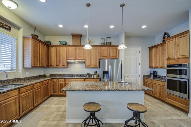 kitchen featuring under cabinet range hood, appliances with stainless steel finishes, brown cabinets, and a sink