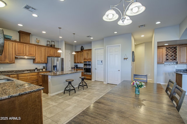 kitchen with brown cabinets, stainless steel appliances, visible vents, under cabinet range hood, and a kitchen bar