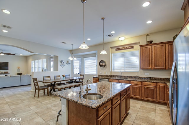 kitchen featuring stainless steel appliances, arched walkways, a sink, and an island with sink