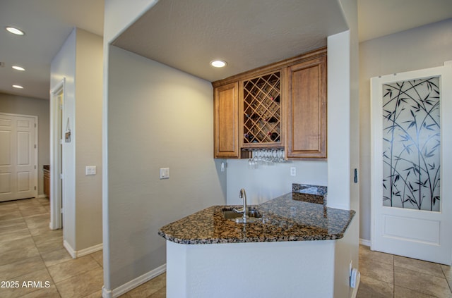 kitchen featuring baseboards, dark stone counters, brown cabinetry, a sink, and recessed lighting