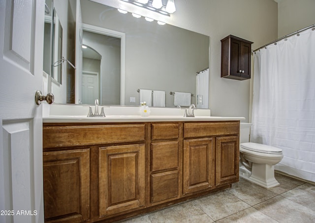 bathroom featuring toilet, double vanity, a sink, and tile patterned floors