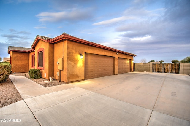 exterior space featuring concrete driveway, an attached garage, a gate, fence, and stucco siding