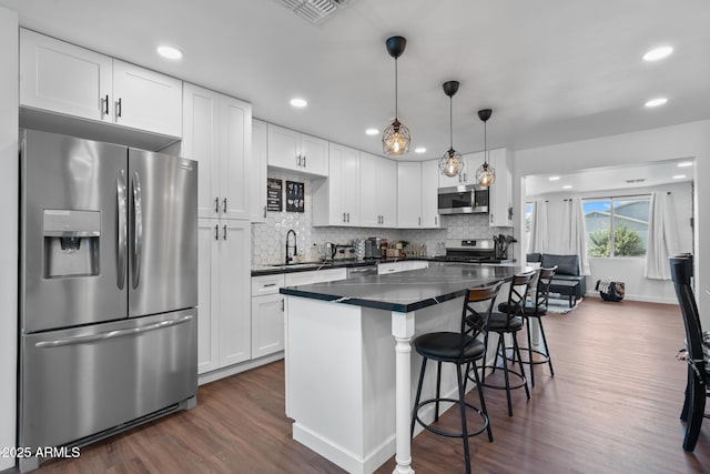 kitchen with decorative light fixtures, appliances with stainless steel finishes, dark hardwood / wood-style flooring, a kitchen breakfast bar, and white cabinets