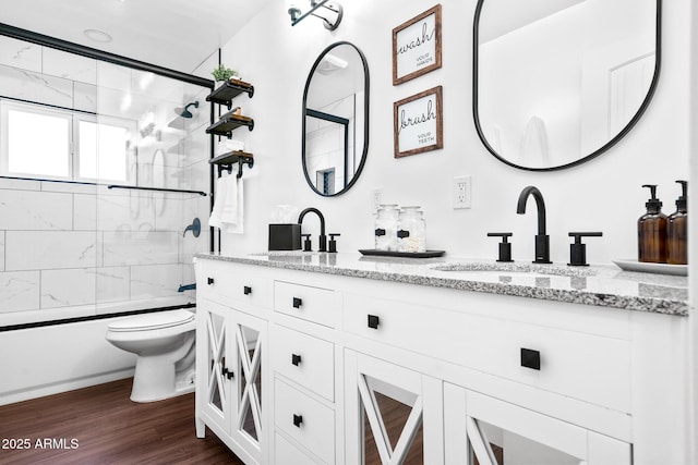 full bathroom featuring vanity, hardwood / wood-style floors, bath / shower combo with glass door, and toilet