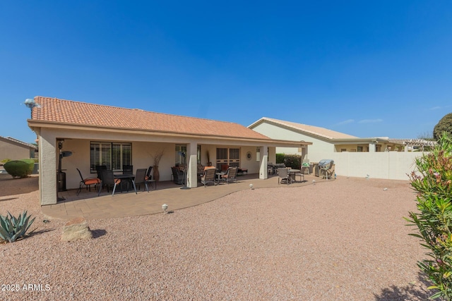 rear view of property with a tile roof, stucco siding, fence, and a patio