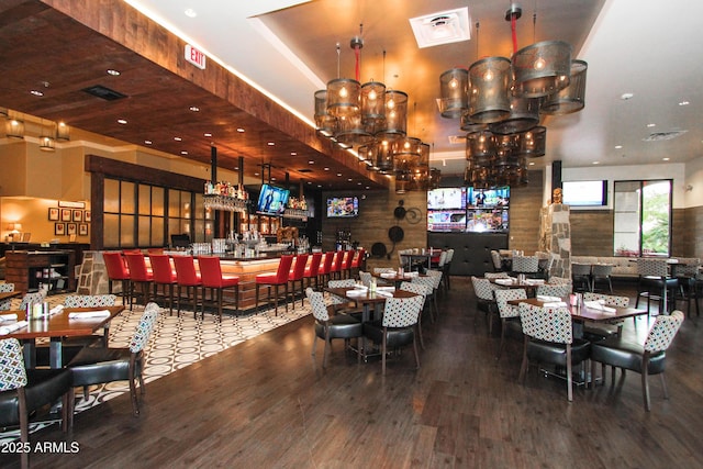 dining space with a community bar, a raised ceiling, visible vents, and wood finished floors