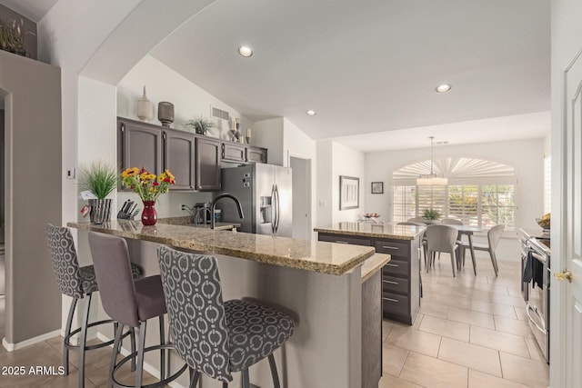 kitchen with a breakfast bar, light tile patterned floors, appliances with stainless steel finishes, light stone countertops, and a peninsula