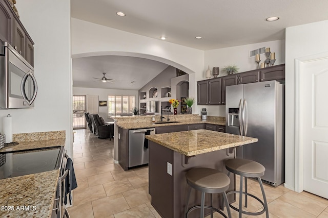 kitchen featuring a peninsula, appliances with stainless steel finishes, light stone counters, and dark brown cabinets