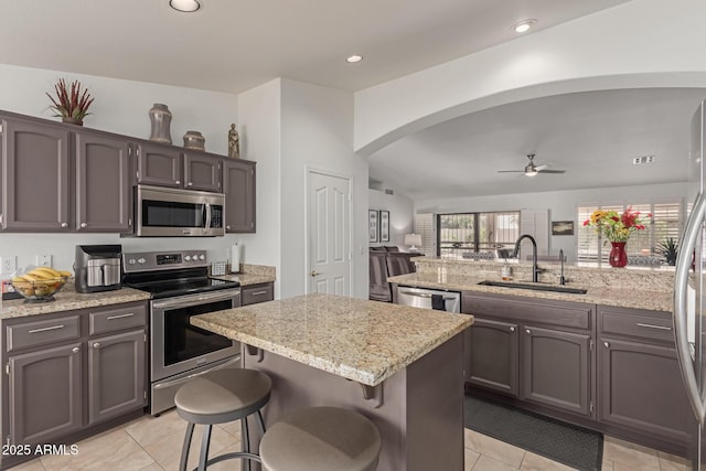 kitchen featuring arched walkways, a center island, appliances with stainless steel finishes, a sink, and a kitchen breakfast bar