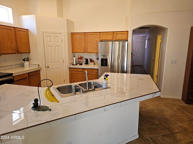 kitchen featuring a towering ceiling, stove, sink, and stainless steel refrigerator with ice dispenser