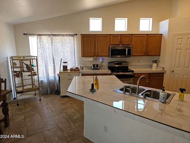 kitchen featuring tile countertops, appliances with stainless steel finishes, sink, and vaulted ceiling