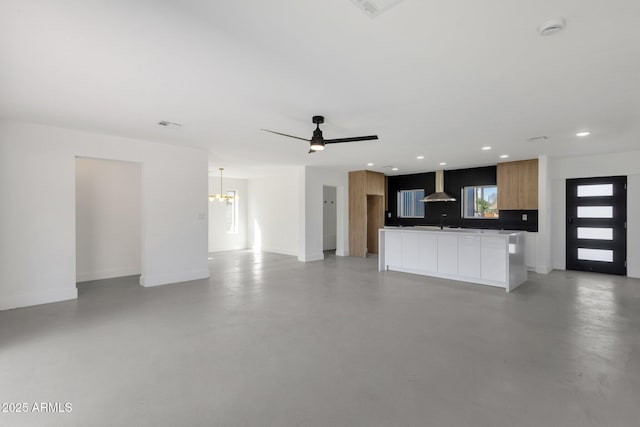 unfurnished living room featuring ceiling fan with notable chandelier, a sink, finished concrete flooring, recessed lighting, and baseboards