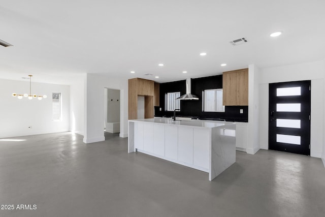 kitchen with modern cabinets, visible vents, concrete flooring, and wall chimney exhaust hood