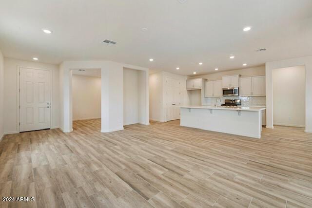 kitchen with a center island with sink, white cabinets, light wood-type flooring, a kitchen bar, and stainless steel appliances