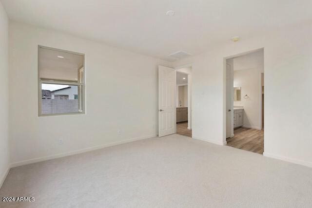 unfurnished bedroom featuring connected bathroom and light colored carpet