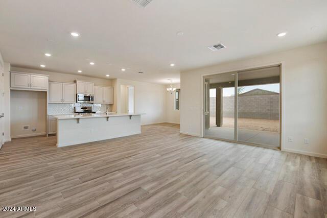 kitchen featuring tasteful backsplash, a kitchen breakfast bar, light hardwood / wood-style flooring, an island with sink, and white cabinets