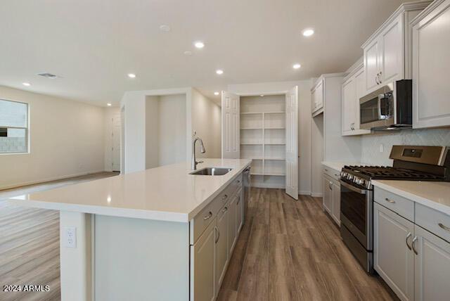 kitchen with stainless steel appliances, a kitchen island with sink, sink, white cabinets, and light hardwood / wood-style floors