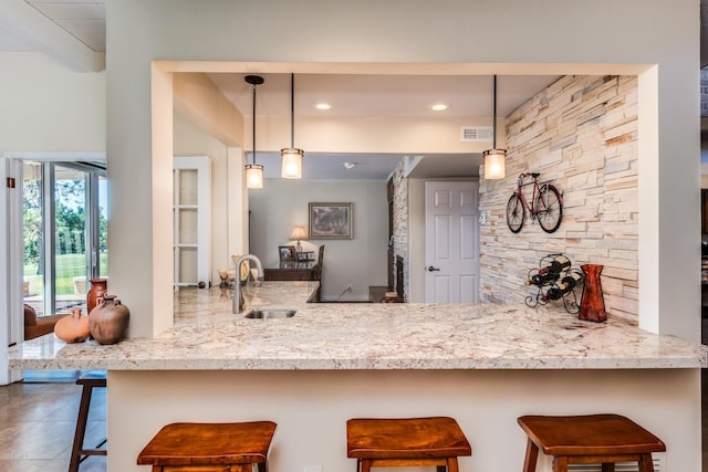 kitchen with visible vents, a kitchen bar, a peninsula, hanging light fixtures, and a sink