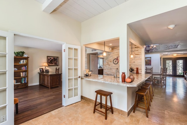 kitchen with light stone counters, french doors, a breakfast bar area, and baseboards