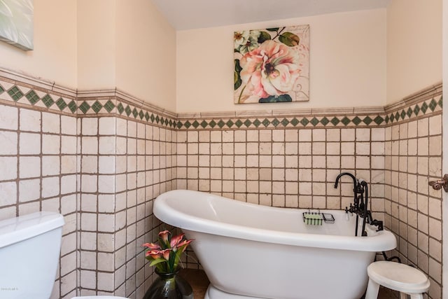 full bath with a wainscoted wall, toilet, tile walls, and a soaking tub