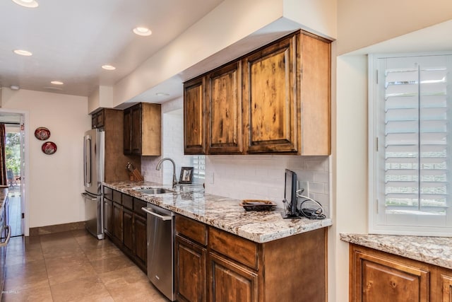 kitchen featuring tasteful backsplash, baseboards, light stone countertops, stainless steel appliances, and a sink