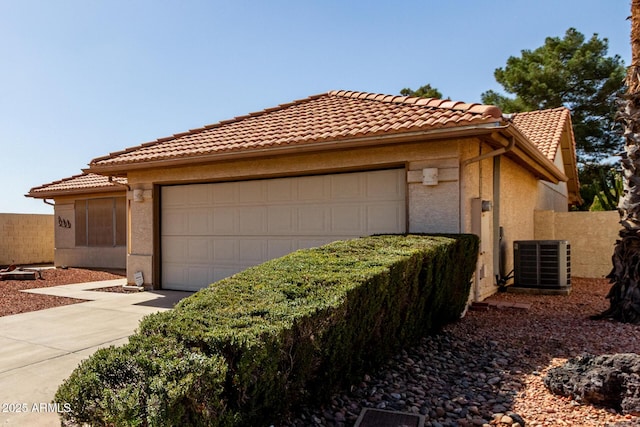 view of side of property with concrete driveway, an attached garage, fence, central AC, and stucco siding