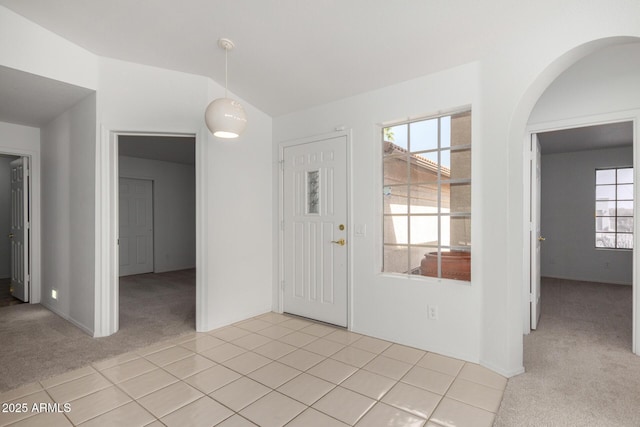 foyer entrance featuring lofted ceiling, light tile patterned floors, plenty of natural light, and light colored carpet