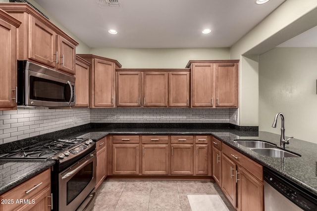 kitchen featuring stainless steel appliances, dark stone counters, brown cabinetry, and a sink