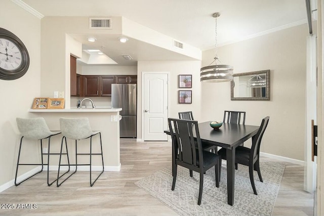 dining area featuring crown molding, sink, an inviting chandelier, and light wood-type flooring