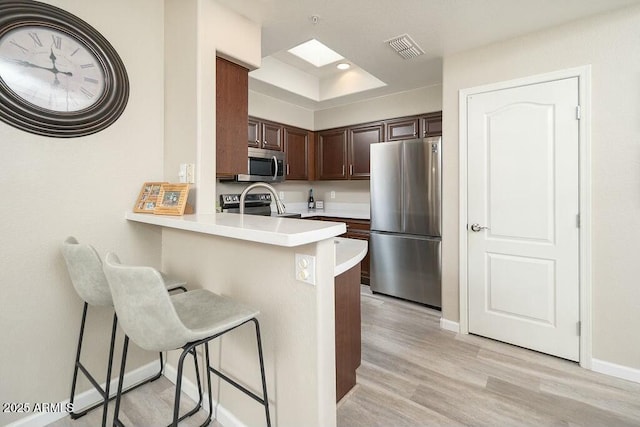 kitchen featuring light hardwood / wood-style floors, stainless steel appliances, a kitchen breakfast bar, and kitchen peninsula