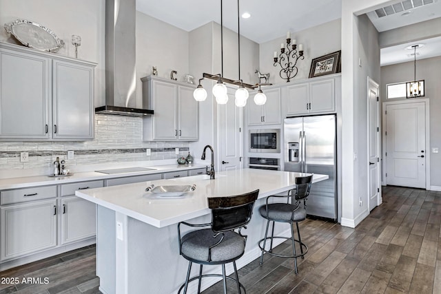 kitchen with a kitchen breakfast bar, stainless steel appliances, wall chimney range hood, pendant lighting, and an island with sink