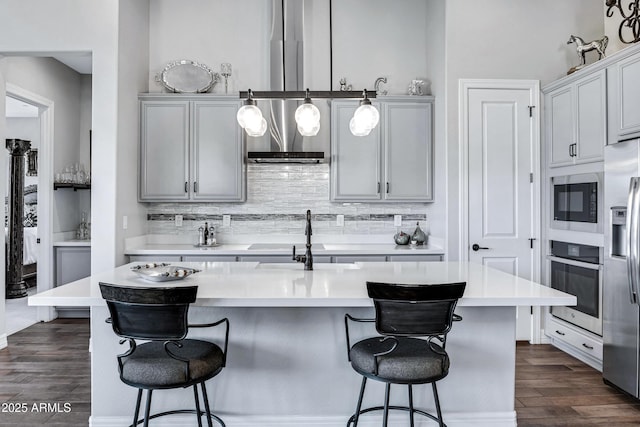 kitchen featuring appliances with stainless steel finishes, dark hardwood / wood-style flooring, pendant lighting, gray cabinets, and an island with sink