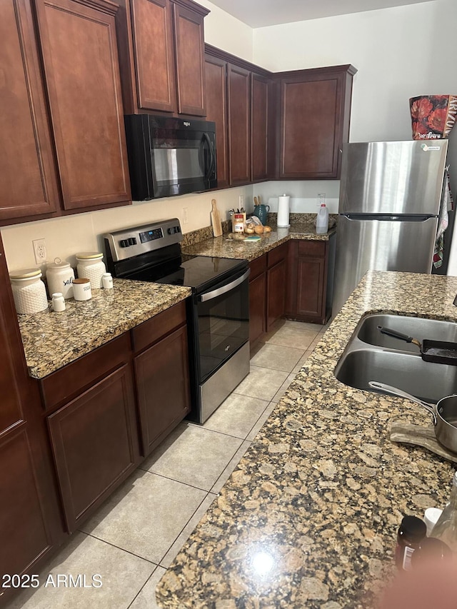 kitchen with light tile patterned floors, stone countertops, stainless steel appliances, and a sink