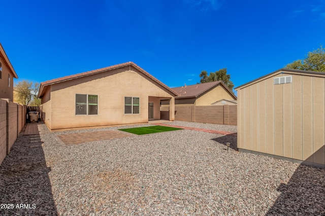 back of house with a storage shed, an outbuilding, a fenced backyard, and stucco siding