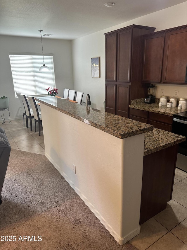 kitchen with visible vents, a center island with sink, stainless steel electric stove, light tile patterned floors, and dark brown cabinets