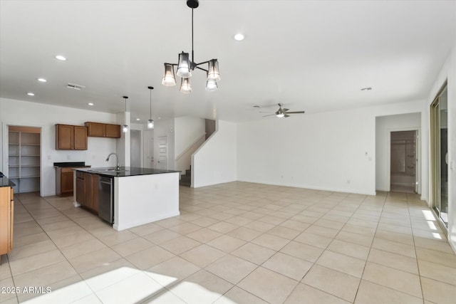 kitchen featuring light tile patterned flooring, hanging light fixtures, stainless steel dishwasher, a kitchen island with sink, and ceiling fan with notable chandelier